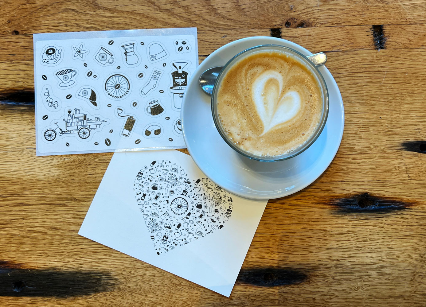 Eine Kaffeetasse von oben mit einer Postkarte und einem Aufkleber-Bogen